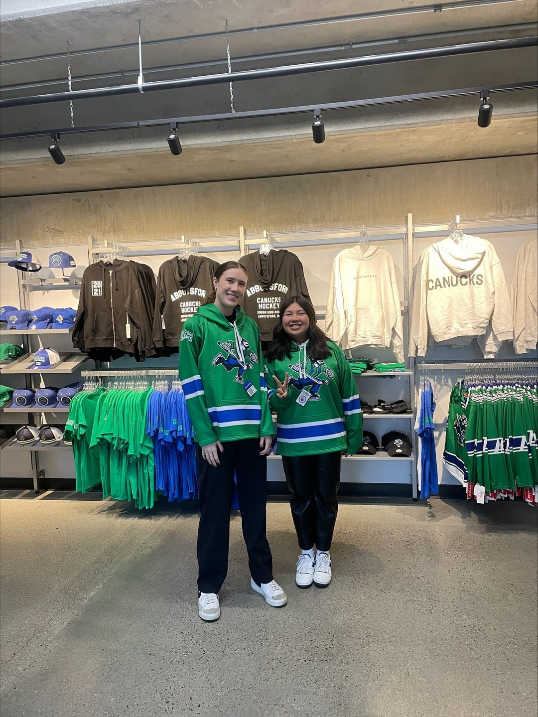 Two fans wearing Bench Clearers Abbotsford Canucks hockey hoodies in the Abbotsford Canucks team store